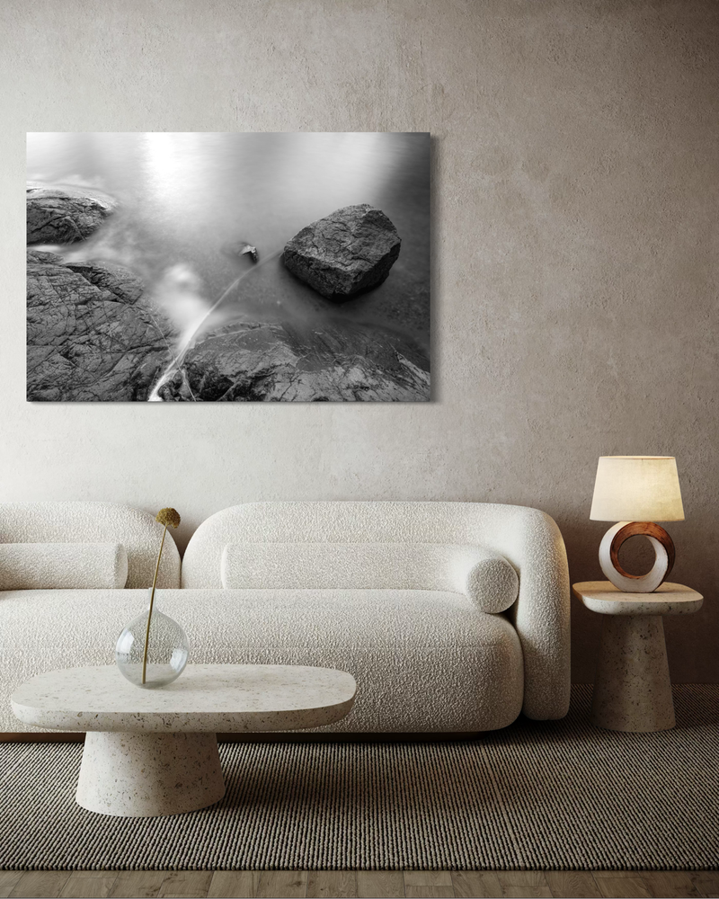 Black-and-white photography on canvas of cliffs and ocean captured with long exposure, where water softly flows around the rocks in a calm composition.