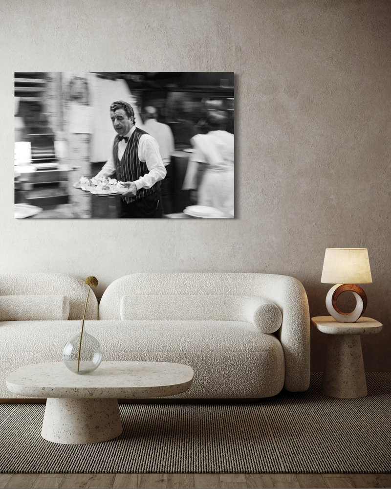 Black-and-white photography on canvas of a waiter in motion carrying a tray through a restaurant setting, with blurred background and a sense of speed.